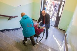 Głosowanie - Paweł Adamowicz wnosi kobietę na wózku do lokalu wyborczego